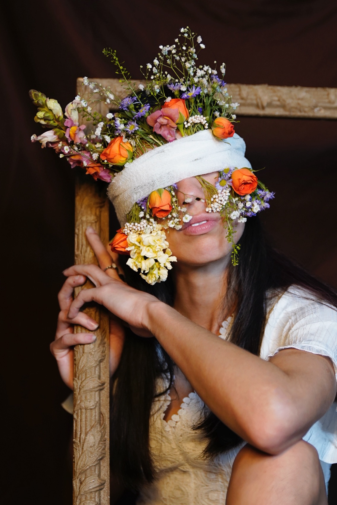 Fine art portrait of a woman in an antique frame, her eyes bound with gauze and a crown of wildflowers across her face