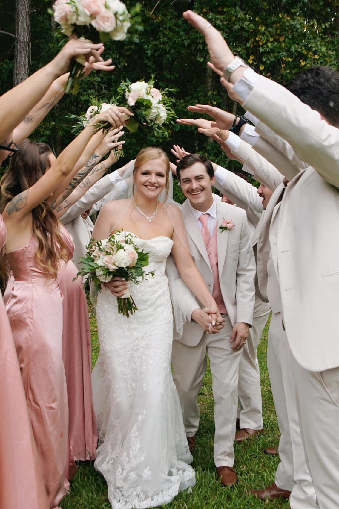 Bride and groom walking hand in hand through a tunnel of raised arms and bouquets held up by their wedding party