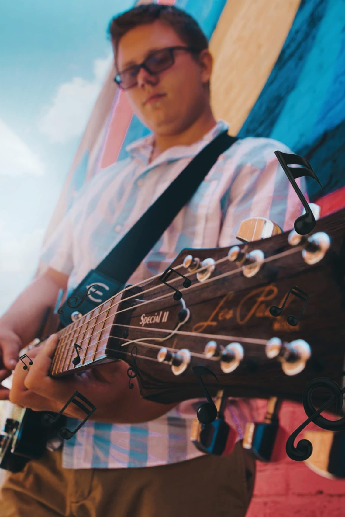 Senior portrait of a young man playing an electric guitar against a painted mural, music notes drifting across the frame